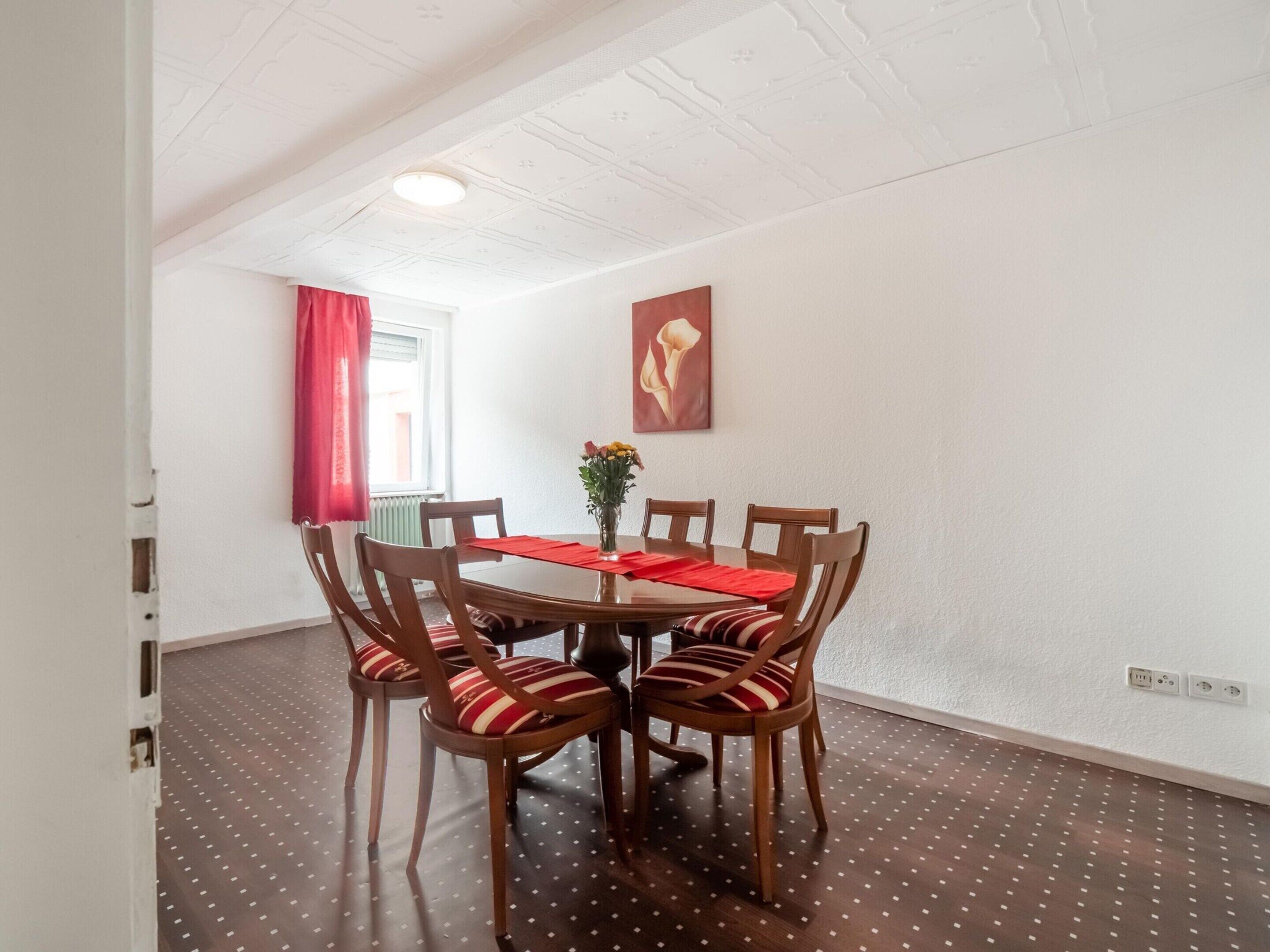 A dining area with a round table, six wooden chairs, and a vase of flowers.