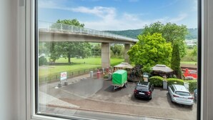 A view from a window overlooking a parking area with a bridge, trees, and a grassy field. - Cheerful Holiday Home in Kinheim With Mountain Views (Kinheim)