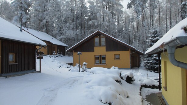 Un chalet enneigé, avec une façade en bois, un espace d’accueil bien visible et un chemin menant à l’entrée.