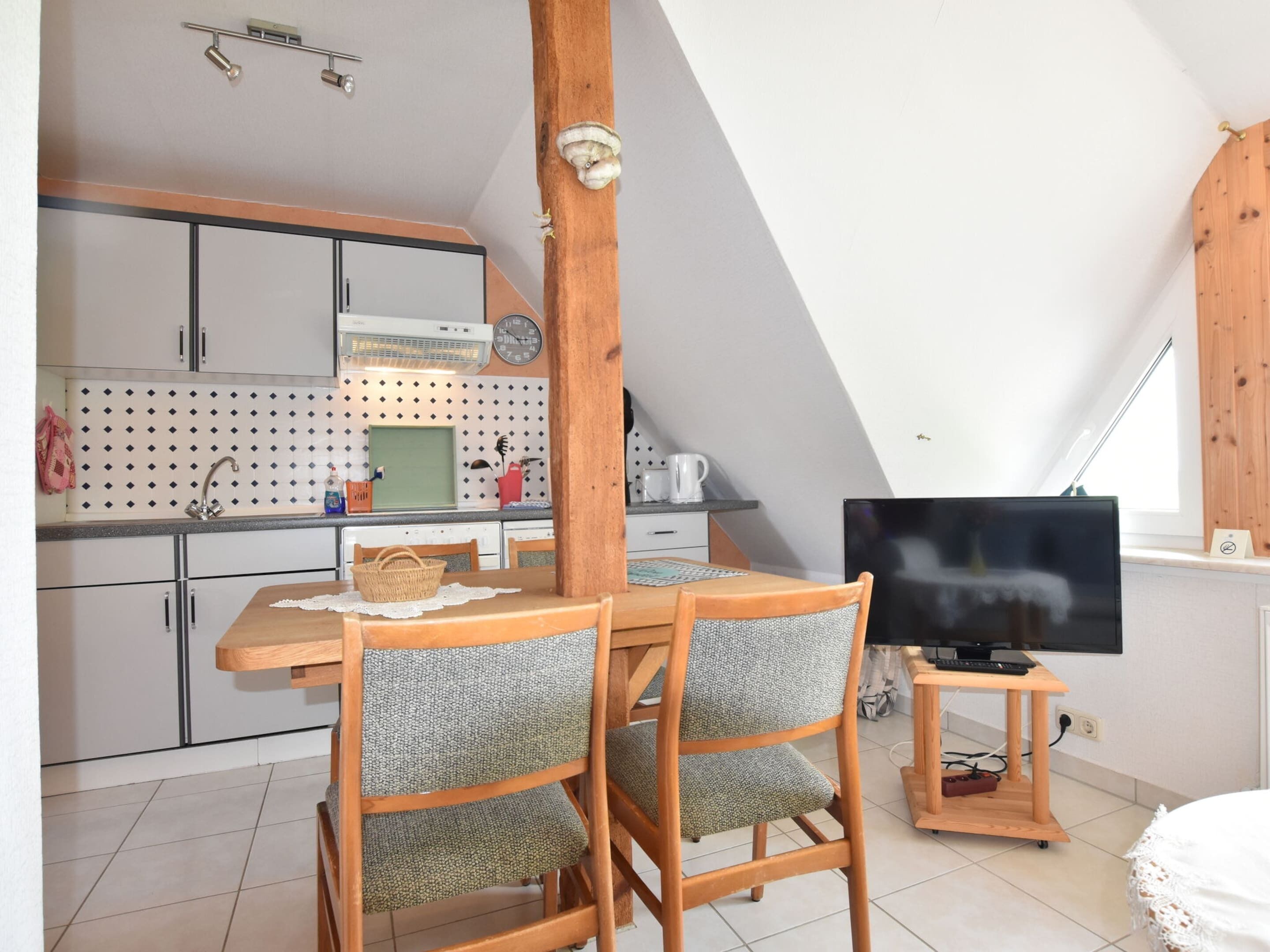 A compact kitchen with white cabinets, a microwave, and a sink. There is a dining table with chairs and a television on a stand.