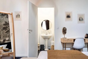 A bedroom with a bed, a desk, a chair, a mirror, a sink, and framed pictures on the walls. - HENRI II  (Le Mans)