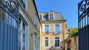 Une cour dallée de pierres, un bâtiment aux volets blancs et un portail bleu.