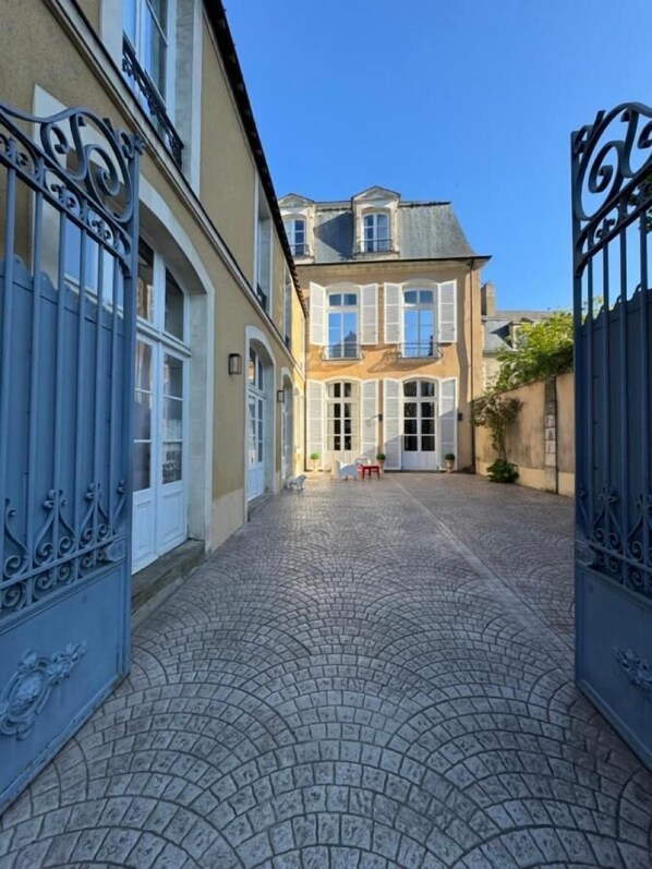 A courtyard with cobblestone paving, a building with white shutters, and a blue gate. - HENRI II  (Le Mans)