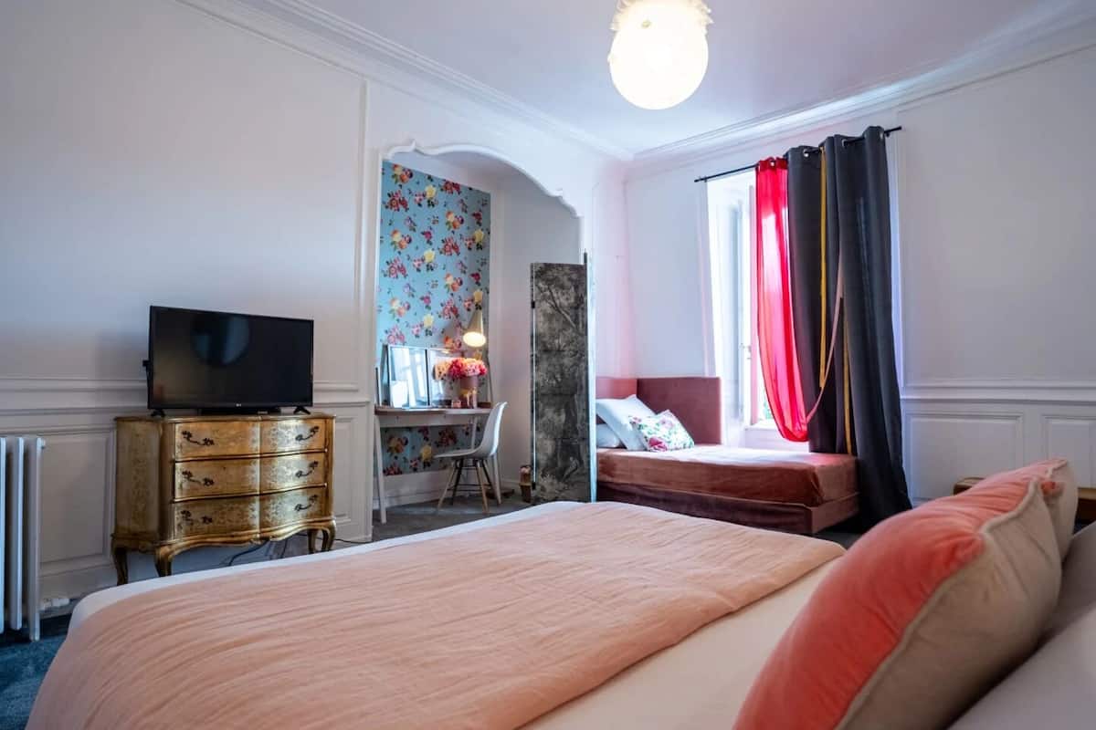 A hotel room with a large bed, a desk with a chair, a television, and a window with curtains.