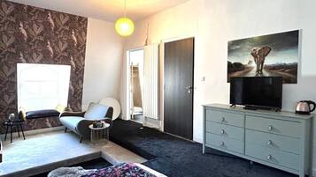 Une chambre à coucher avec un lit, un canapé, un téléviseur posé sur une commode et un tableau accroché au mur.