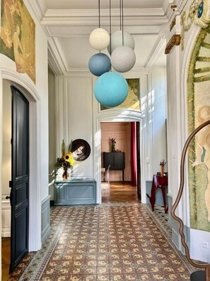 A hallway with patterned flooring, a blue console table, a black cabinet, and a red side table. - HENRI II  (Le Mans)