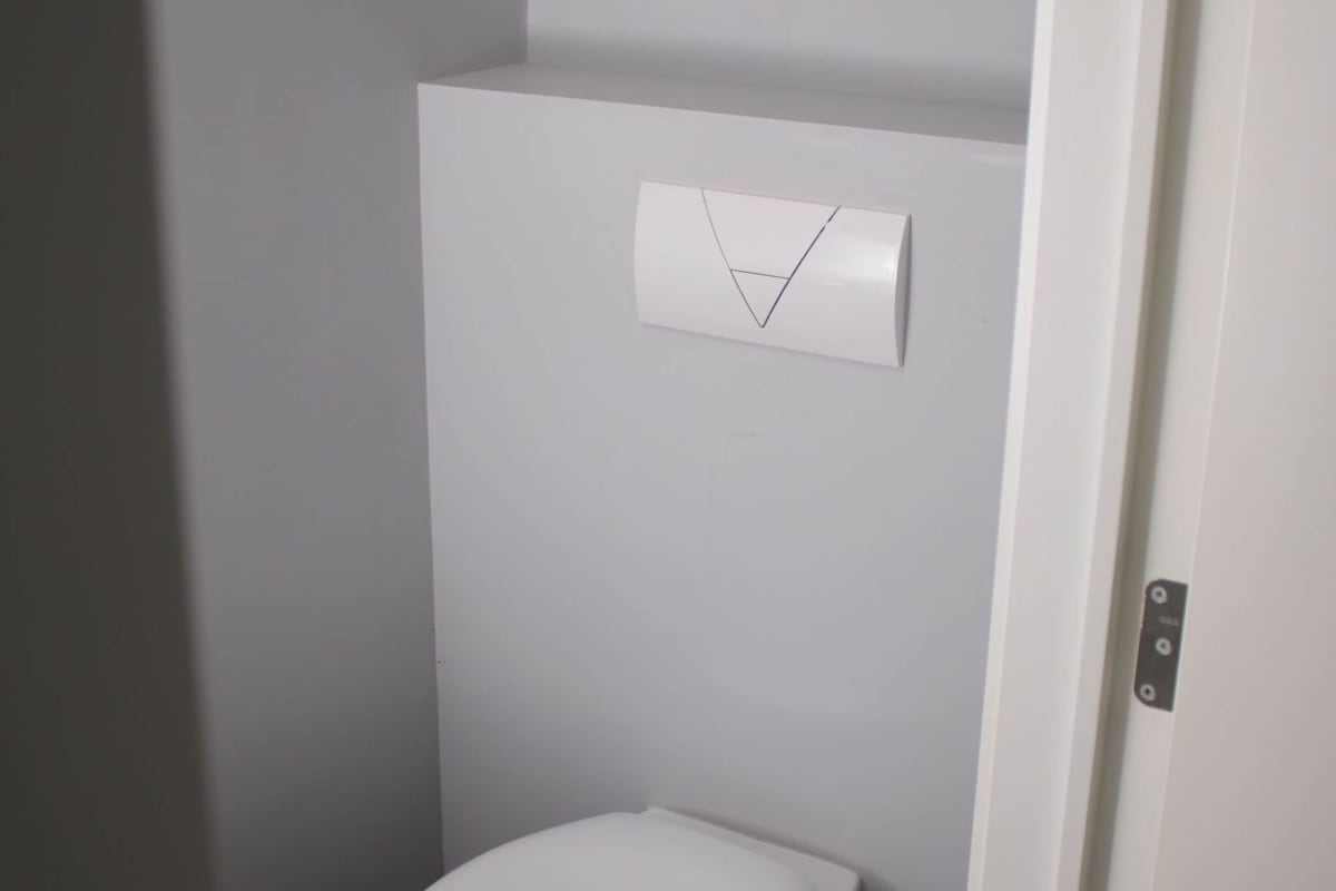 A bathroom with a white toilet, a white wall, and a white door.
