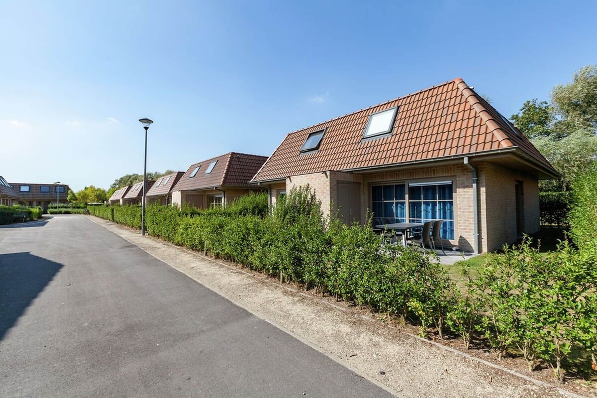 Une rangée de maisons modernes, dotées de toits inclinés et de grandes fenêtres, avec une allée pavée et une haie bien entretenue le long de la rue.