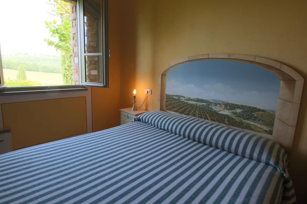 A bedroom with a bed, a nightstand, a lamp, and a mural on the wall.