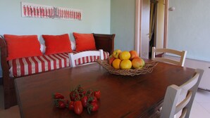 A dining area with a wooden table, a woven fruit basket, and a sofa with red cushions. - Beautiful Farmhouse in San Gimignano With Pool (San Gimignano)
