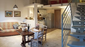 A spacious living area with a dining table set for four, a sofa, and a staircase leading to an upper level. - Beautiful Farmhouse in San Gimignano With Pool (San Gimignano)
