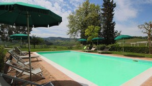 A swimming pool with lounge chairs and umbrellas, surrounded by greenery and hills. - Beautiful Farmhouse in San Gimignano With Pool (San Gimignano)