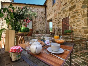 Un bâtiment rustique en pierre, avec une table en bois dressée pour le petit-déjeuner.