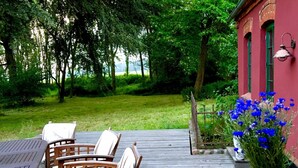 Eine Holzterrasse mit Gartenmöbeln, einem Blumentopf und einem Gebäude mit grünen Fenstern.