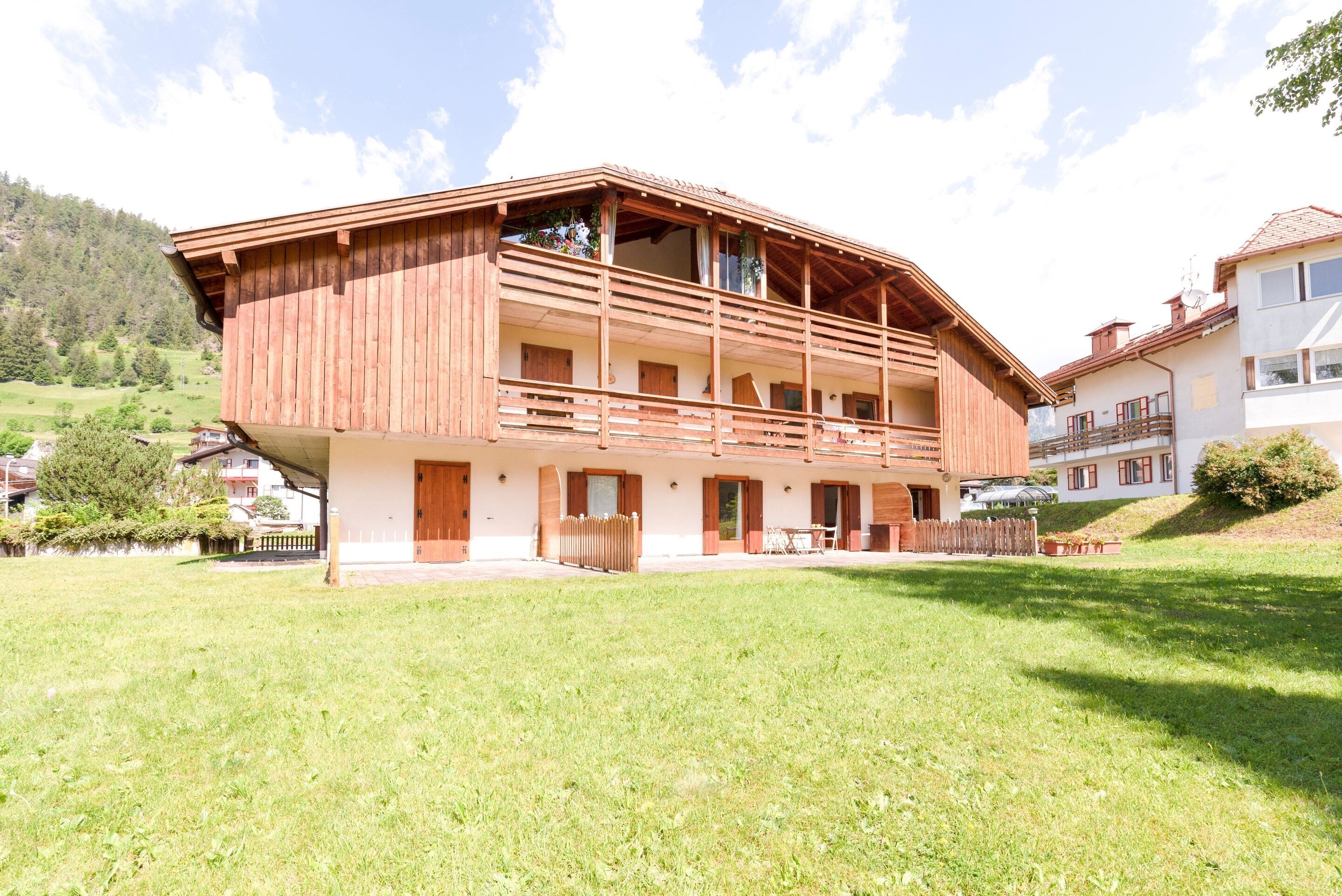 Un chalet de madera con balcón, rodeado de césped y con una montaña al fondo.