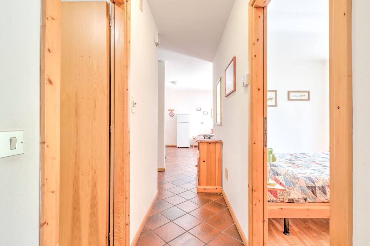 A narrow hallway with wooden doors leading to a bedroom with a bed and a small desk.