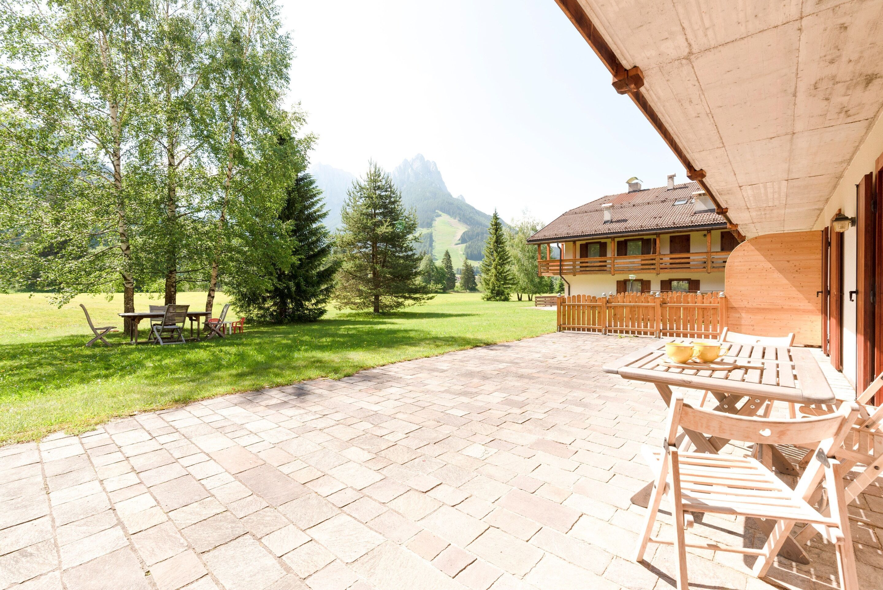 Un patio con muebles de madera, vistas a la montaña y un edificio con balcón de madera.