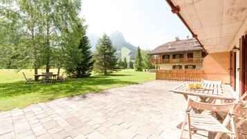 Un patio con muebles de madera, vistas a la montaña y un edificio con balcón de madera.