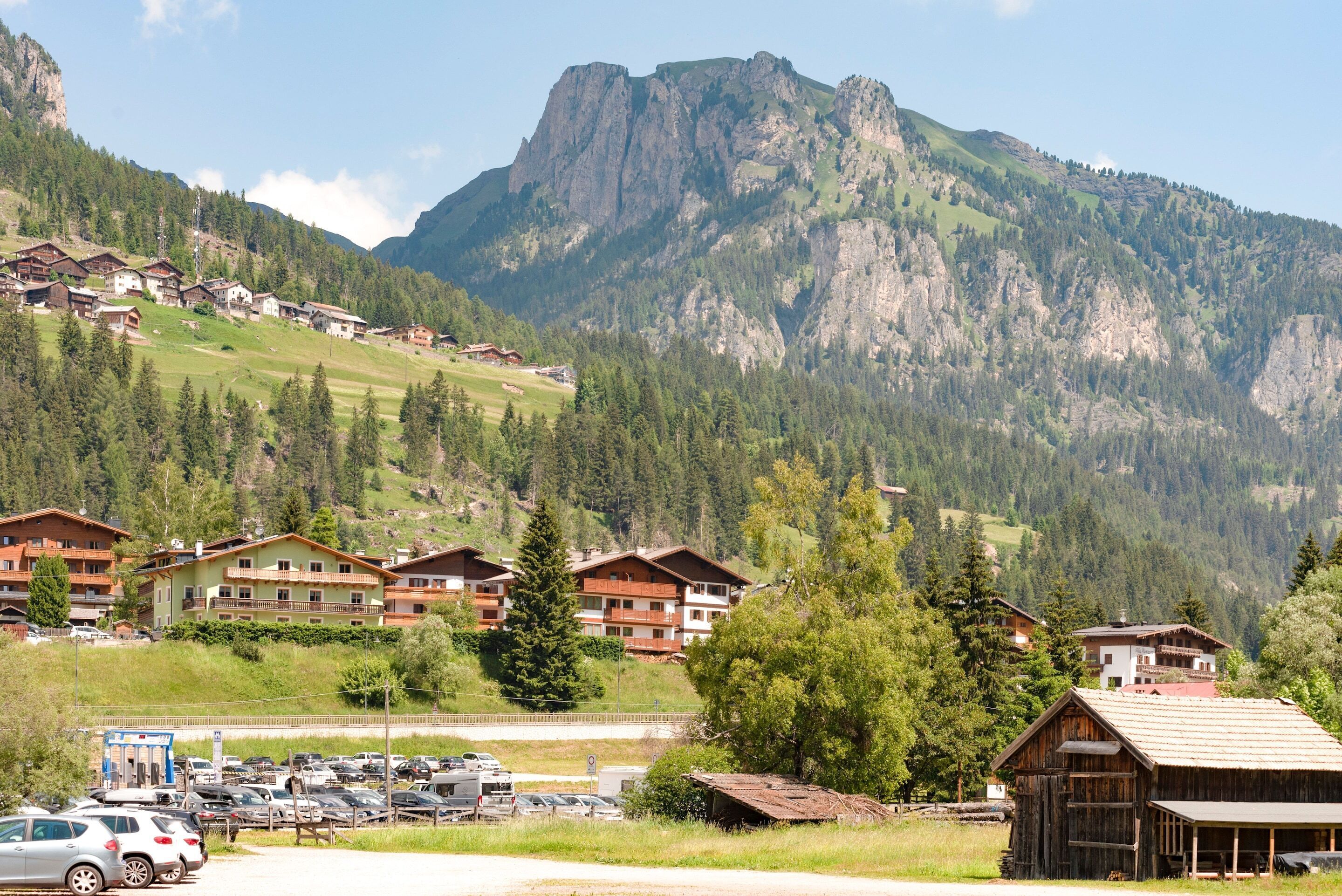 A mountain village with chalet-style buildings, a parking lot, and a prominent rocky mountain in the background.
