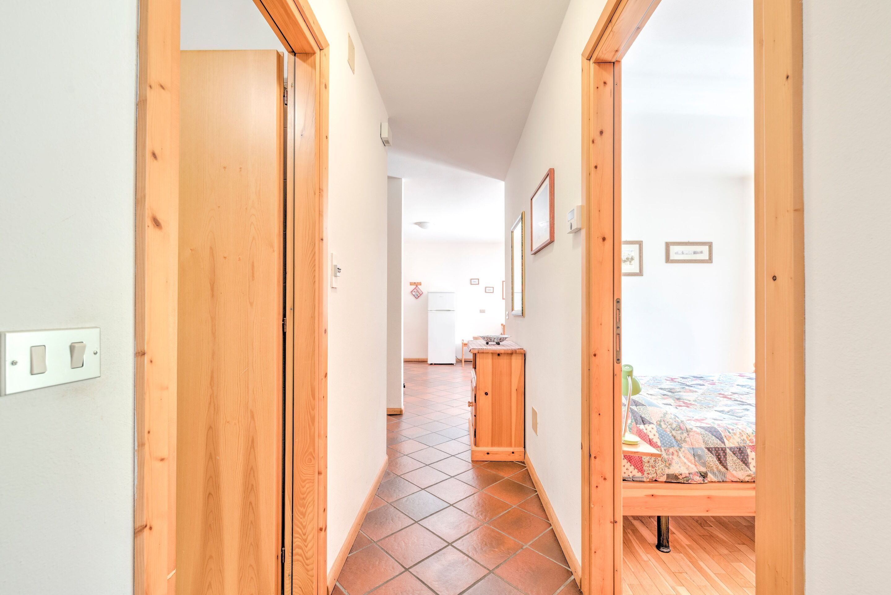 Un pasillo estrecho con puertas de madera que dan a un dormitorio con cama y una mesita de noche pequeña.