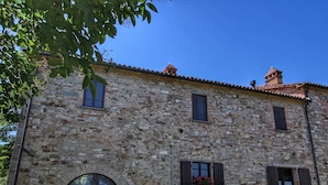 Un bâtiment en pierre avec un toit recouvert de tuiles, deux fenêtres et une porte.