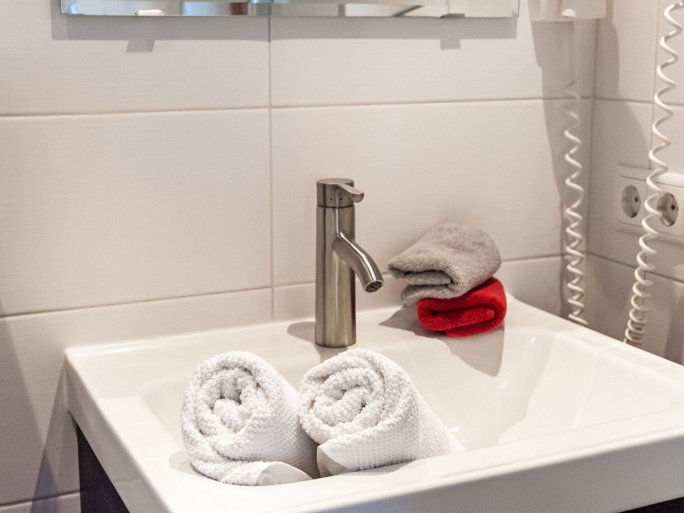 A bathroom sink with two white towels and one red towel.