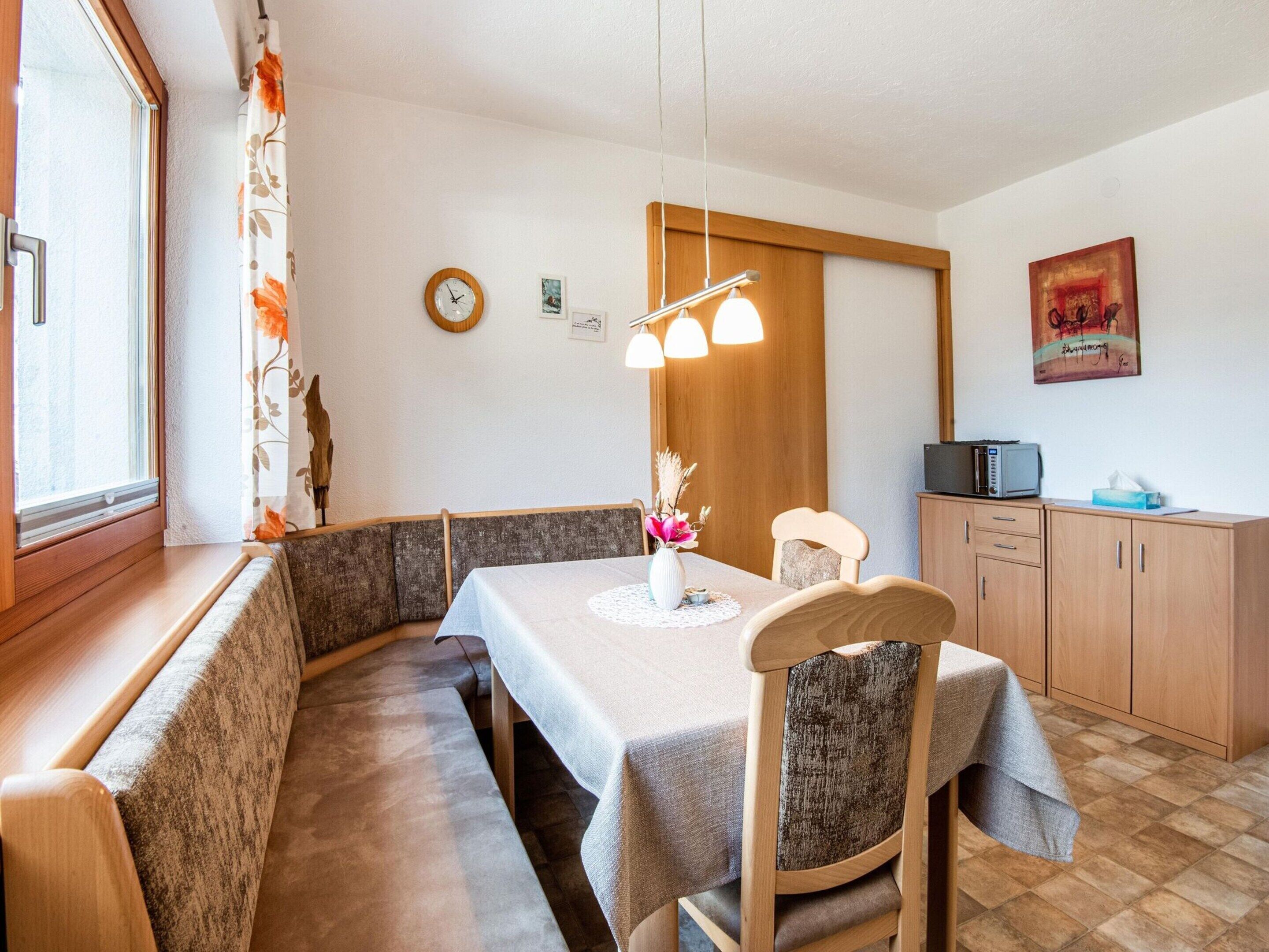 Un coin repas accueillant avec un banc en bois, une table recouverte d’une nappe blanche et un luminaire suspendu moderne.