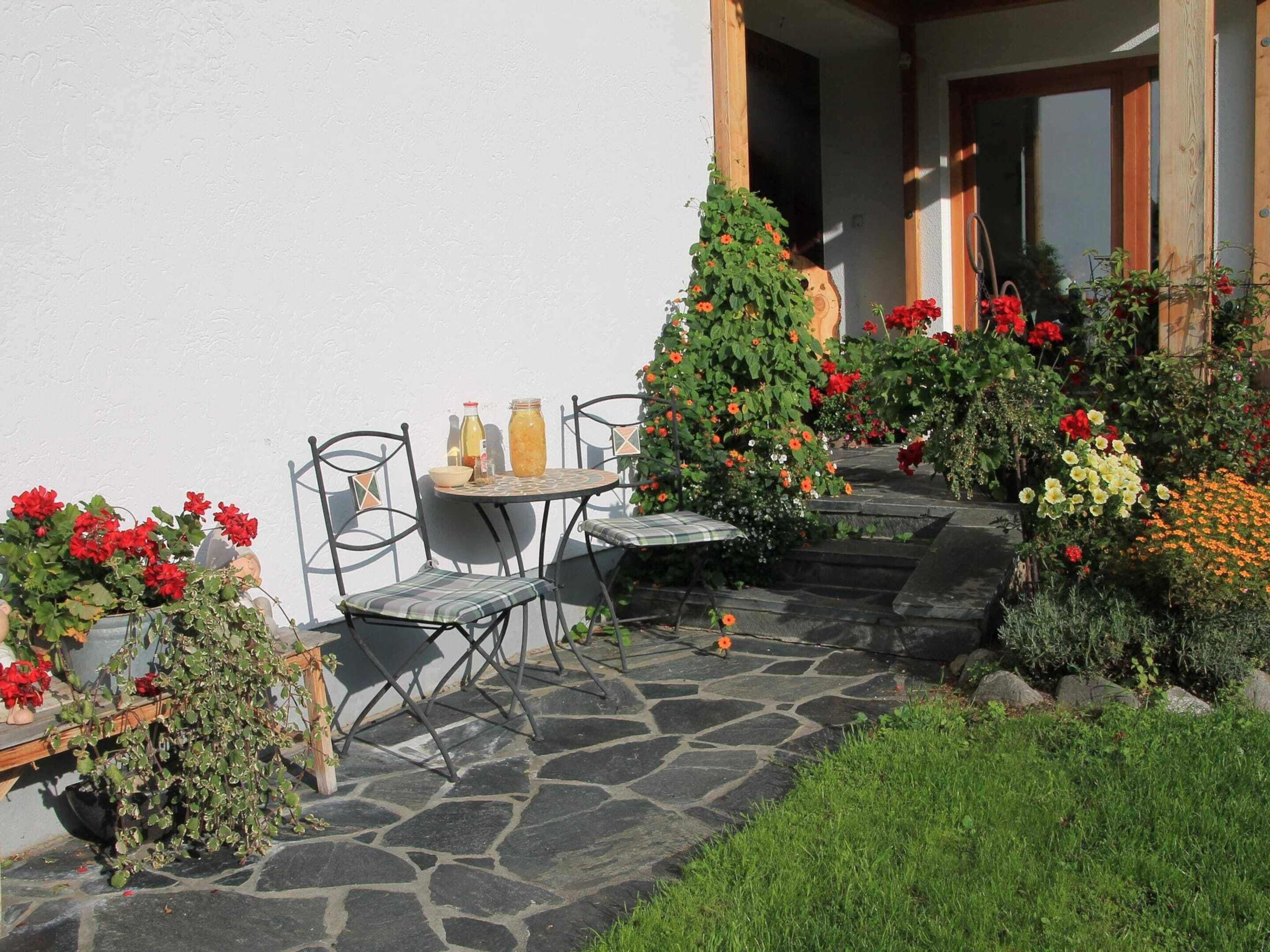 A stone patio with a table and chairs, surrounded by various potted plants and flowers.