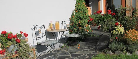 A stone patio with a table and chairs, surrounded by various potted plants and flowers.
