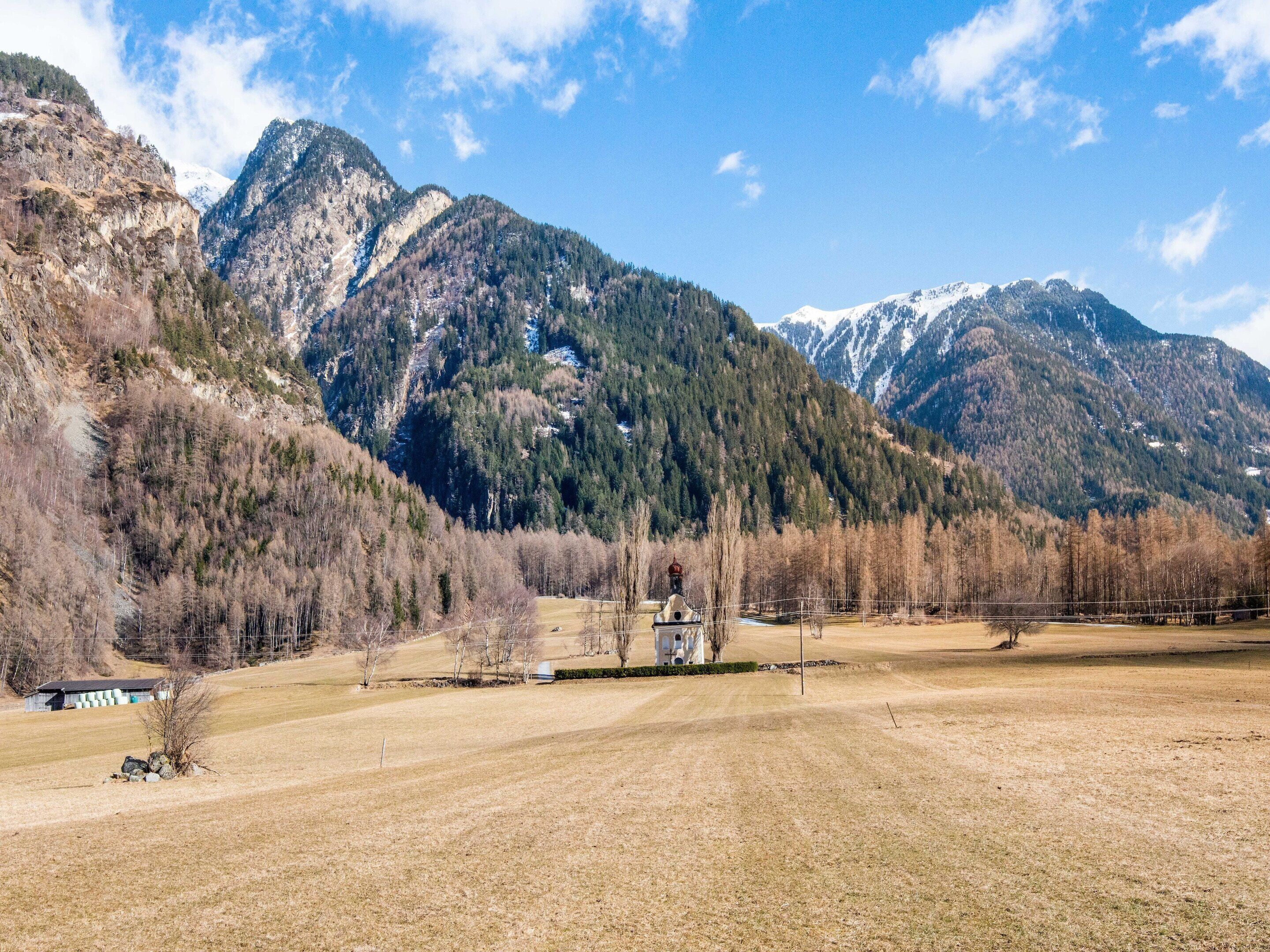 A rural landscape with mountains, a field, and a small building.