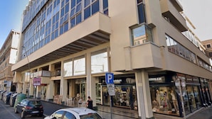 Un immeuble à plusieurs étages doté de grandes fenêtres, de devantures de magasins, dont une boutique de vêtements, et d’un panneau indiquant un parking.
