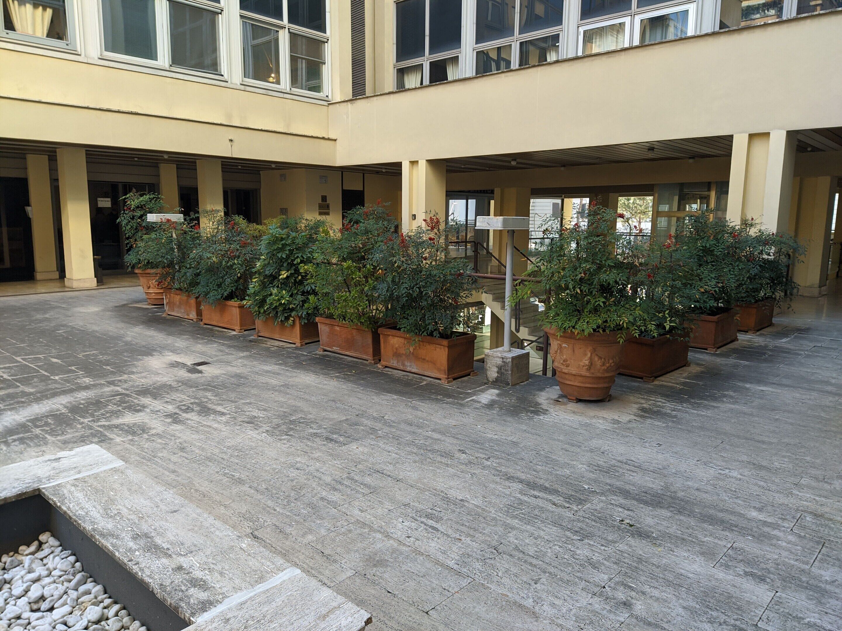 A spacious indoor courtyard with a tiled floor, surrounded by potted plants and a central water feature.