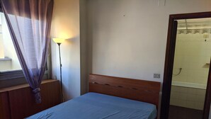 Une chambre à coucher avec un lit simple, une table de chevet, une lampe et une fenêtre avec des rideaux.