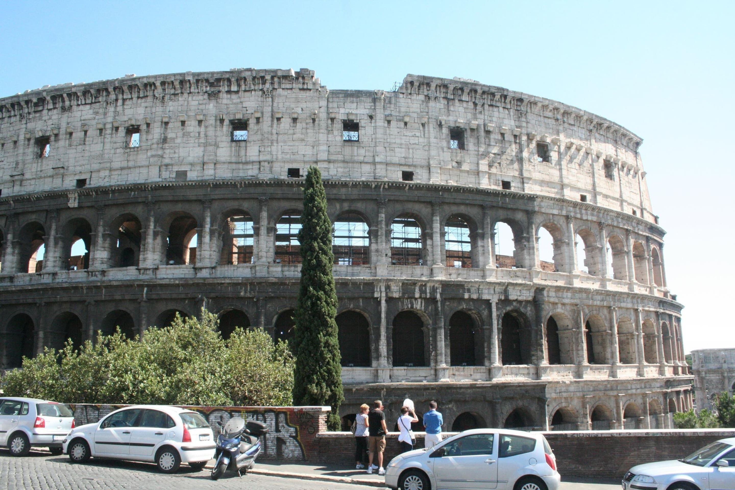 A historic amphitheater with multiple levels of arches and a crowd of people in front.