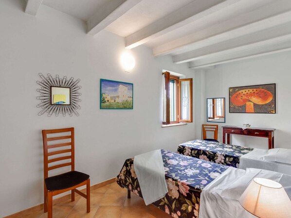 A room with two beds, a wooden chair, a desk, and a wall with three framed pictures.