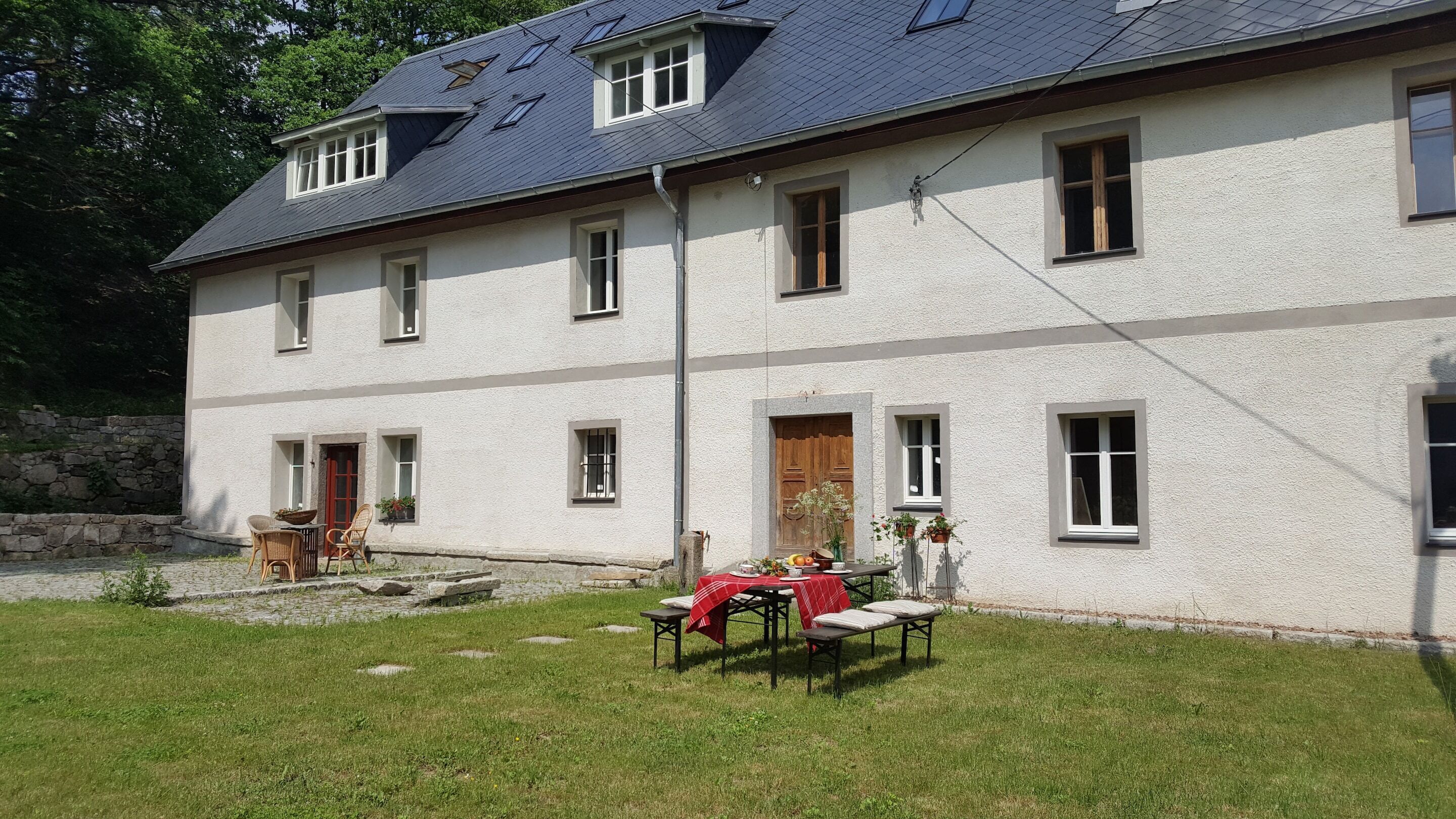 A two-story building with a sloped roof, multiple windows, and a stone wall in the background.