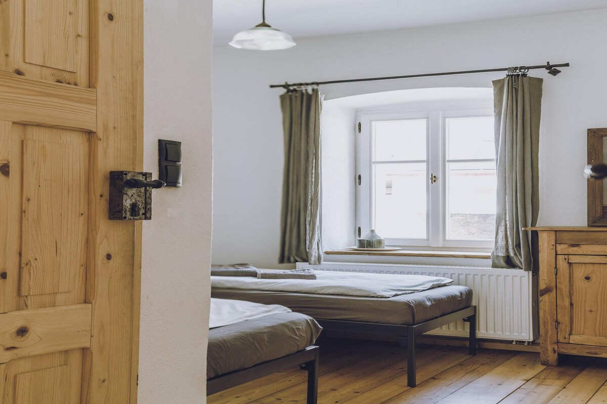 Une chambre avec deux lits, une fenêtre avec des rideaux, un radiateur et une armoire en bois.