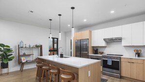 A modern kitchen with a central island, bar stools, stainless steel appliances, and wooden cabinetry. - Luxury in The Gulch with Patio & Pool- Walk to Broadway (Nashville)