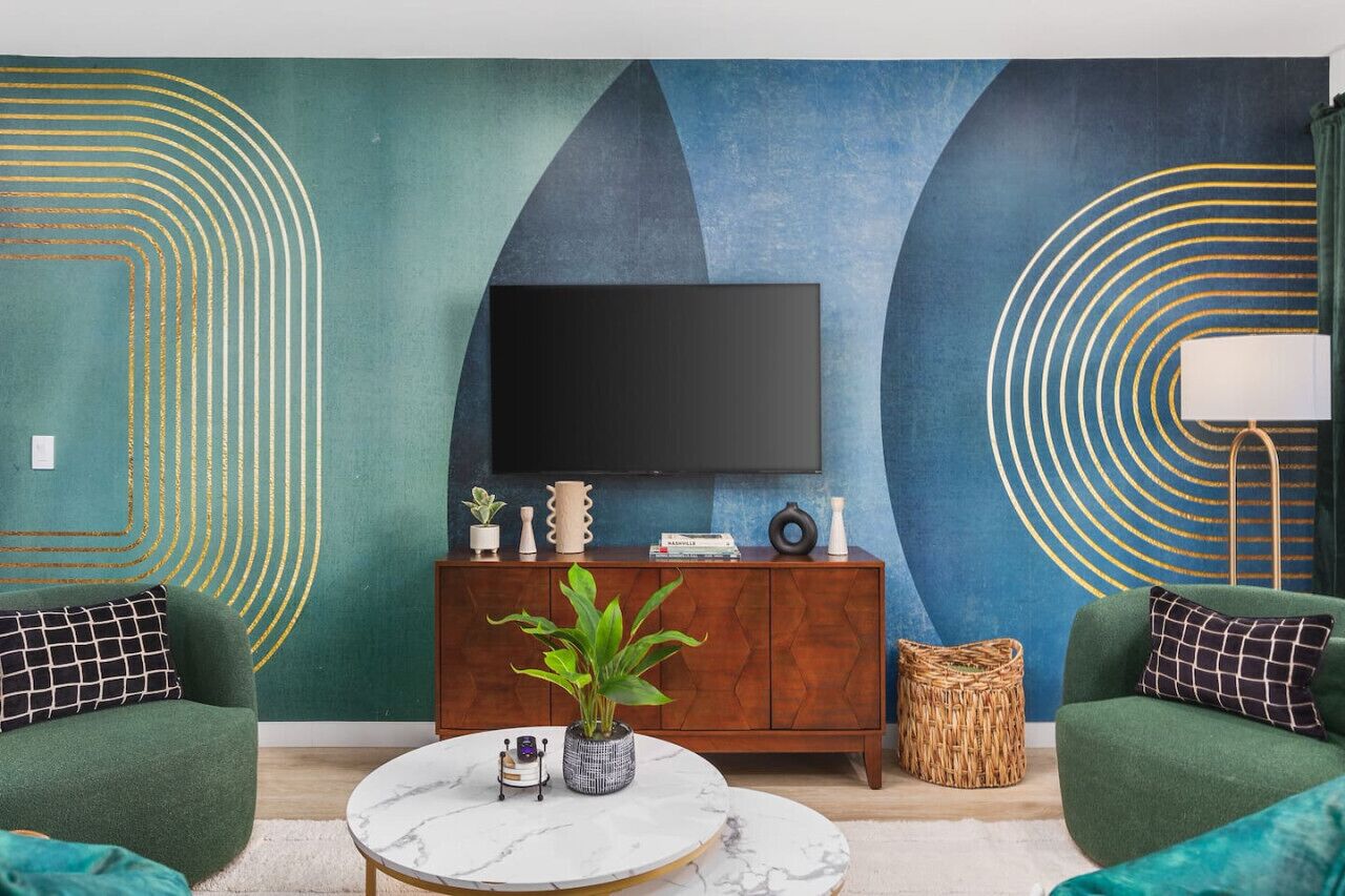 A modern living room with a large flat-screen TV mounted on the wall, a wooden cabinet with decorative items, and two green sofas.