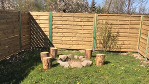 Ein von einer Hecke umgebener Gartenbereich mit einer Holzhütte, Holzstämmen und vereinzelten Steinen.