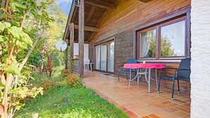 A wooden cabin with a patio area featuring a table and chairs, surrounded by a garden and a large window. - Chalet in Iselsberg-stronach Near Ski-lift (Iselsberg-Stronach)