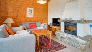 A cozy living room with a stone fireplace, wooden ceiling, and a television on a wooden stand. - Chalet in Iselsberg-stronach Near Ski-lift (Iselsberg-Stronach)