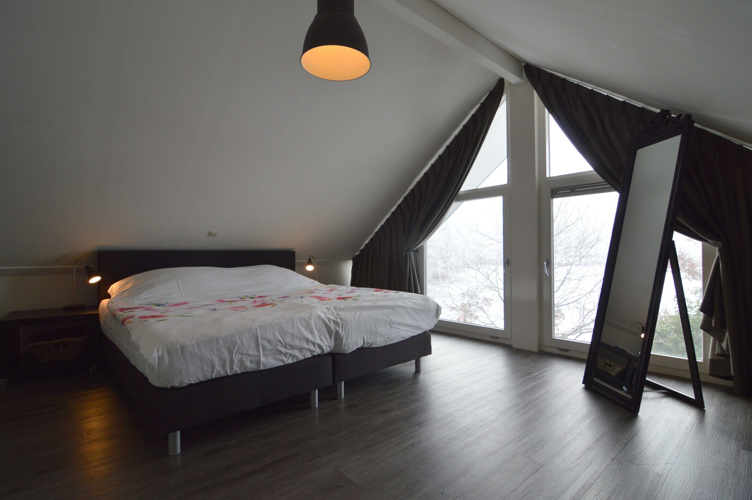 Ein Schlafzimmer mit einem großen Bett, einer Stehlampe und Blick ins Freie durch ein Fenster.