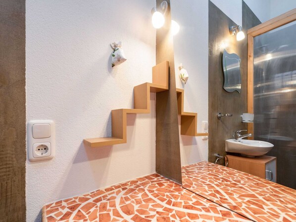A bathroom with a patterned floor, a wooden shelf structure, a mirror, and a sink.