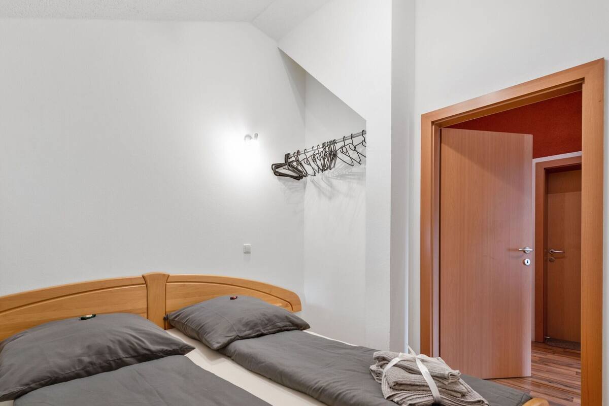 A bedroom with a wooden bed, grey bedding, a towel on the bed, and a door to the right.