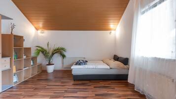 A room with a wooden ceiling, a bed with pillows, a radiator, a bookshelf, and a potted plant.