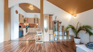 Eine moderne Küche mit Holzausbau, einer Mikrowelle und einem Spülbecken. Ein weißer Stuhl und ein Regal mit Dekorationen sind ebenfalls vorhanden.