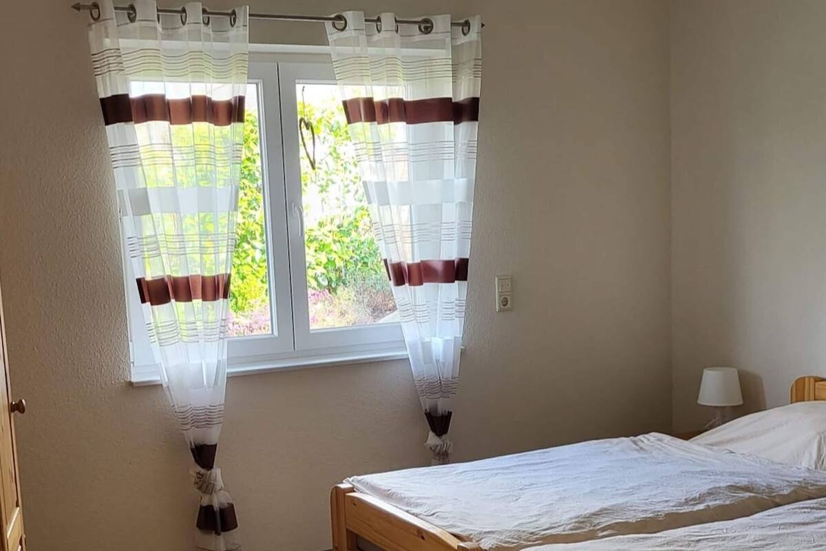 A bedroom with two beds, a window with curtains, and a lamp on the nightstand.