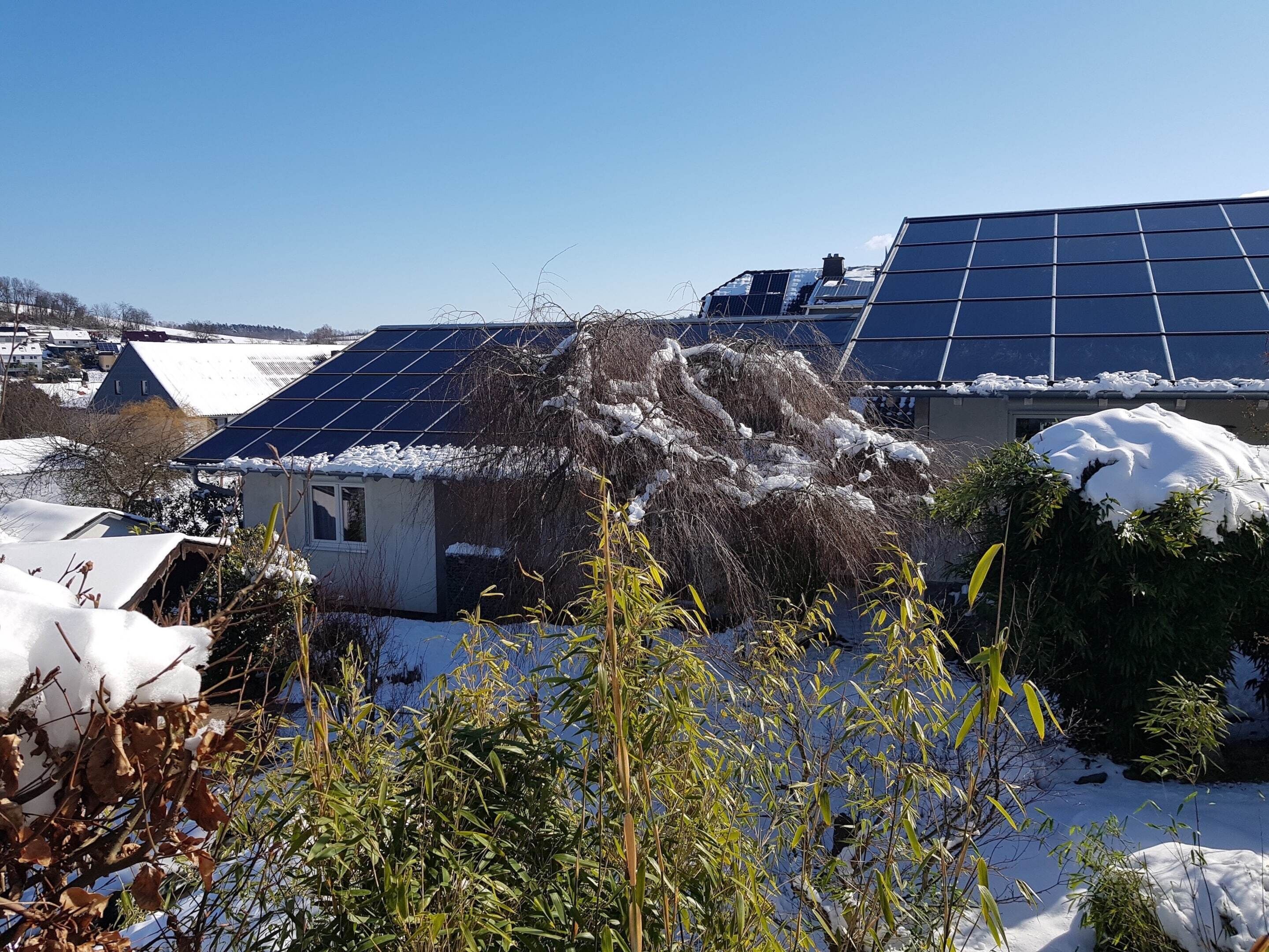 Un quartier résidentiel avec des panneaux solaires sur les toits, une cour enneigée et une petite maison.