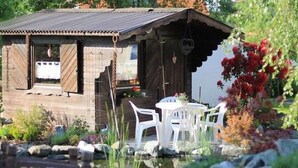 A rustic wooden cabin with a small patio area, surrounded by rocks and plants. - Relaxing Holiday Home in Willersdorf in the Forest (Frankenberg)